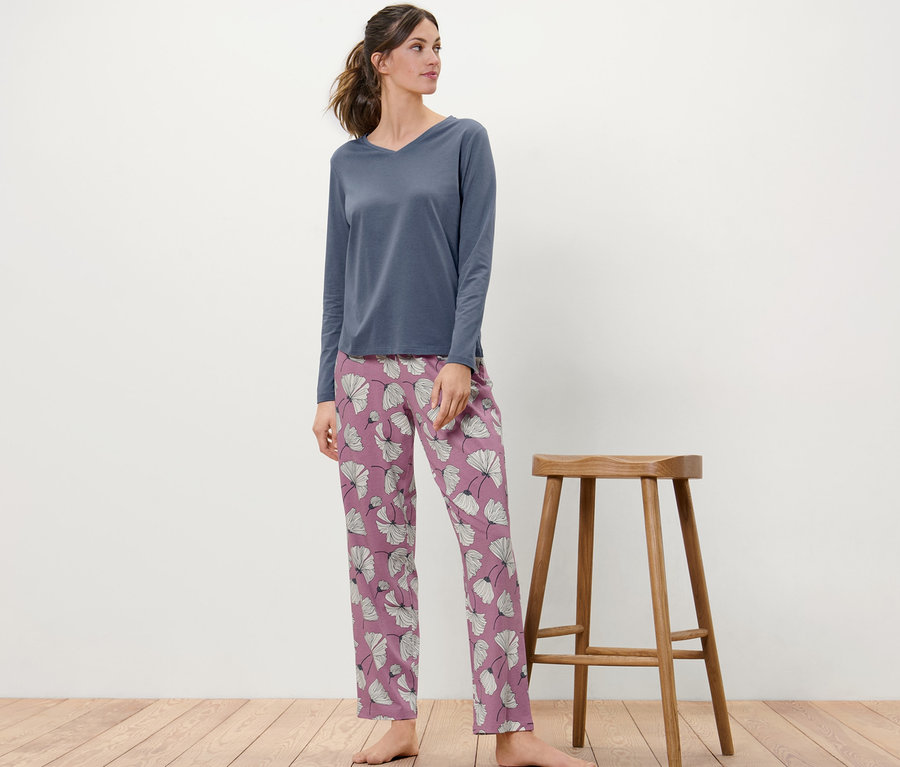 Frau steht neben einem Holzstuhl und trägt einen Pyjama mit Blumenmuster.