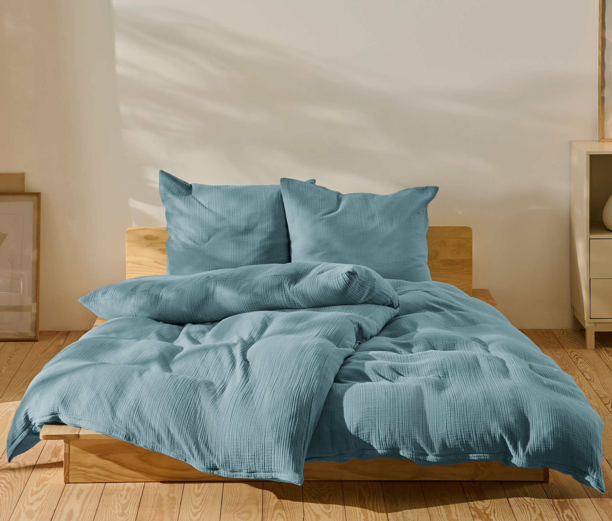 Blaue Musselin-Bettwäsche in Normalgröße und Übergröße auf einem Bett.