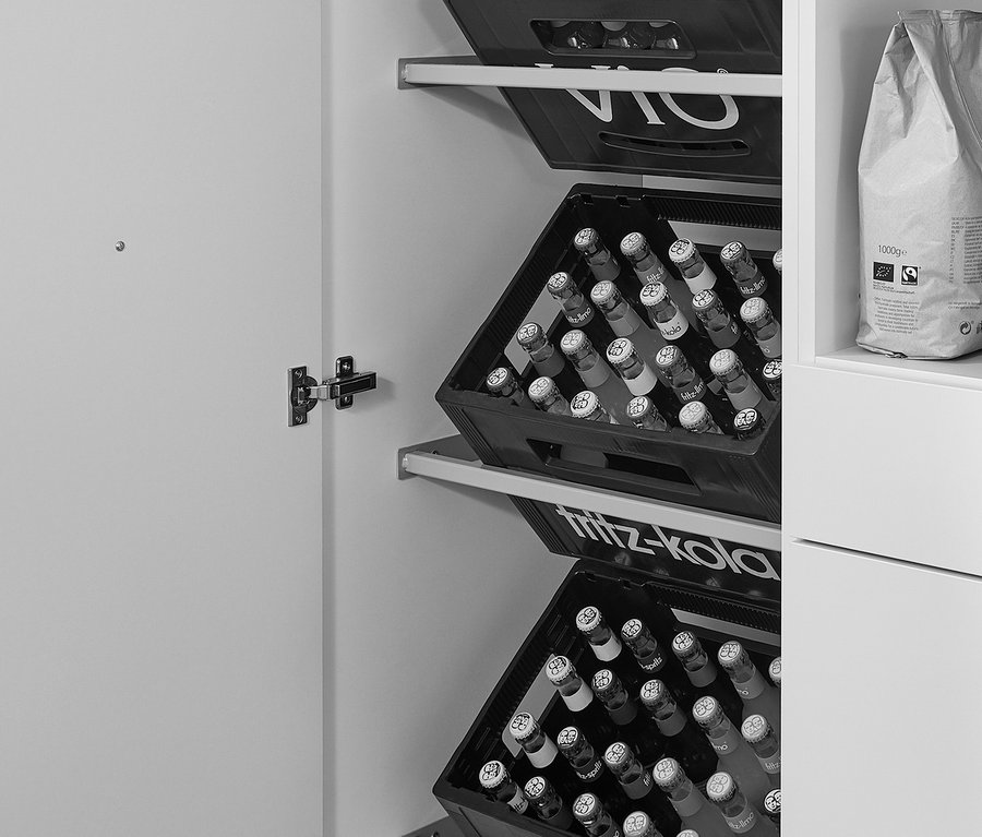 Schwarz-Weiß-Fotografie eines Schrankinneren mit geöffneter Tür, in dem Getränkekisten gelagert werden. Im Schrank sind Seitenschrankmodule für Getränkekisten, links und rechts, in Kieselgrau und Weiß.