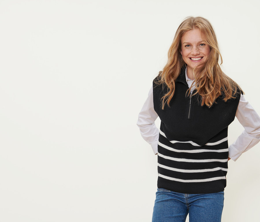 Frau lächelt und trägt einen schwarz-gestreiften Pullunder im Troyer-Stil.