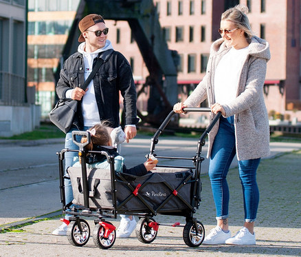 Eine Frau schiebt einen grauen Pinolino Klappbollerwagen Add Plus, in dem ein Kind sitzt, während ein Mann neben ihnen hergeht.