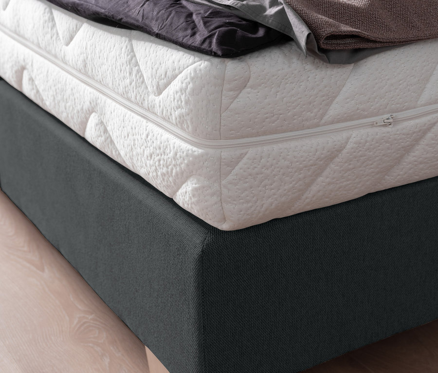 Detailansicht eines Boxspringbetts »DAVINA« mit einer gelben Strickdecke darüber.
