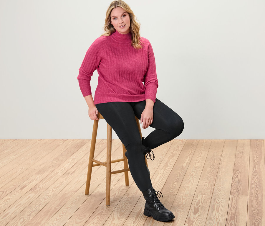 Frau sitzt auf einem Hocker und trägt einen gerippten Strickpullover mit Stehkragen und Thermoleggings.