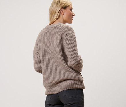 Frau von hinten in taupem Gerippter Grobstrick-Cardigan, dunkle Jeans und Turnschuhe.