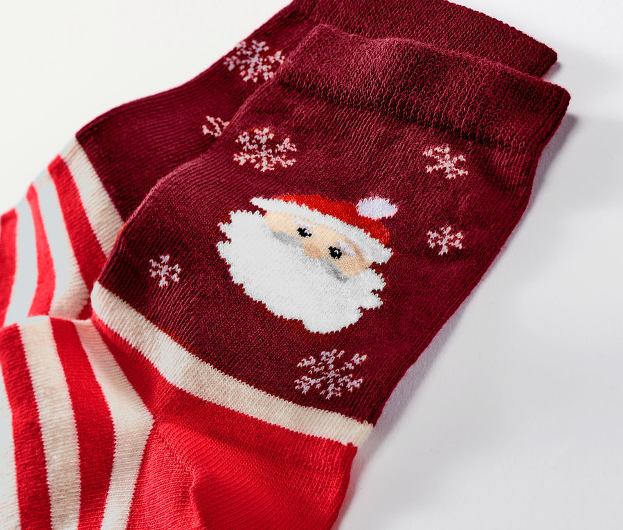 Detailaufnahme von einem Paar Weihnachtssocken in Burgunderrot mit Weihnachtsmann- und Schneeflockenmotiven.