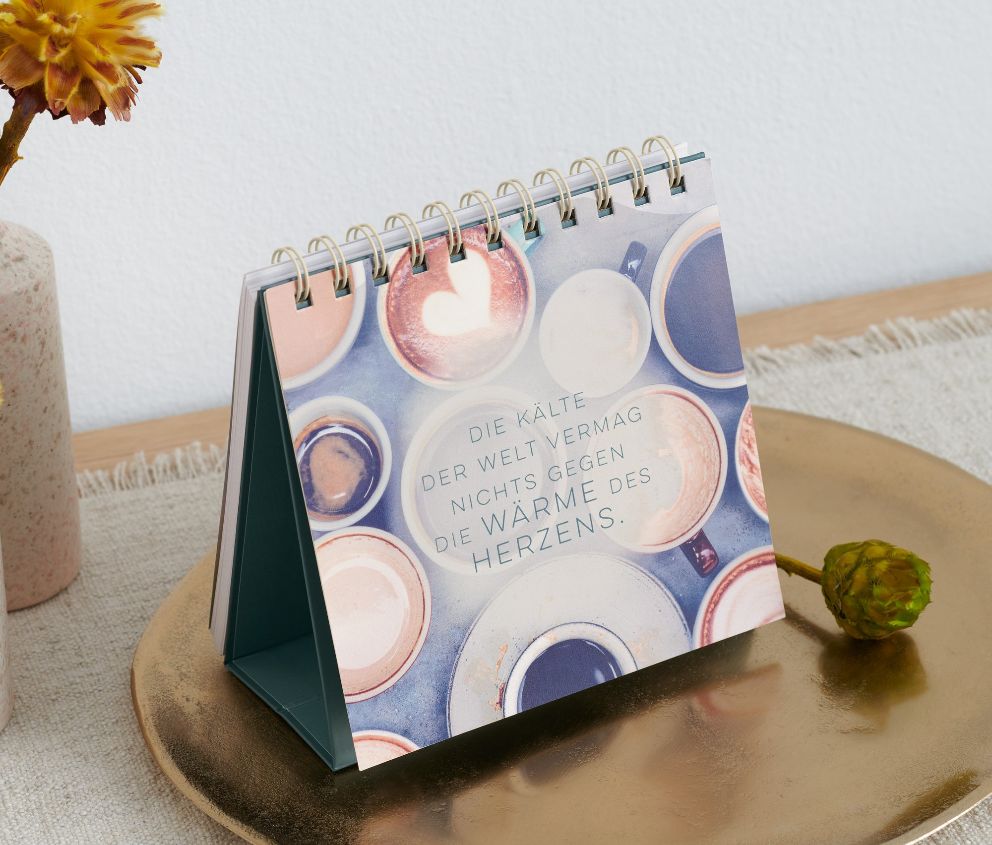 Buch-Tisch-Aufsteller »Mach jeden Tag magisch« steht auf einem goldenen Teller neben Vasen mit Blumen.