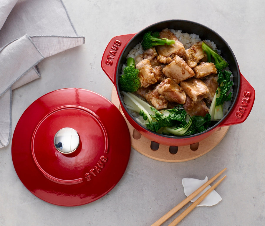 Ein roter STAUB Kochtopf »La Cocotte« mit 16 cm Durchmesser steht mit Deckel neben Reis mit Hühnchen und Gemüse.
