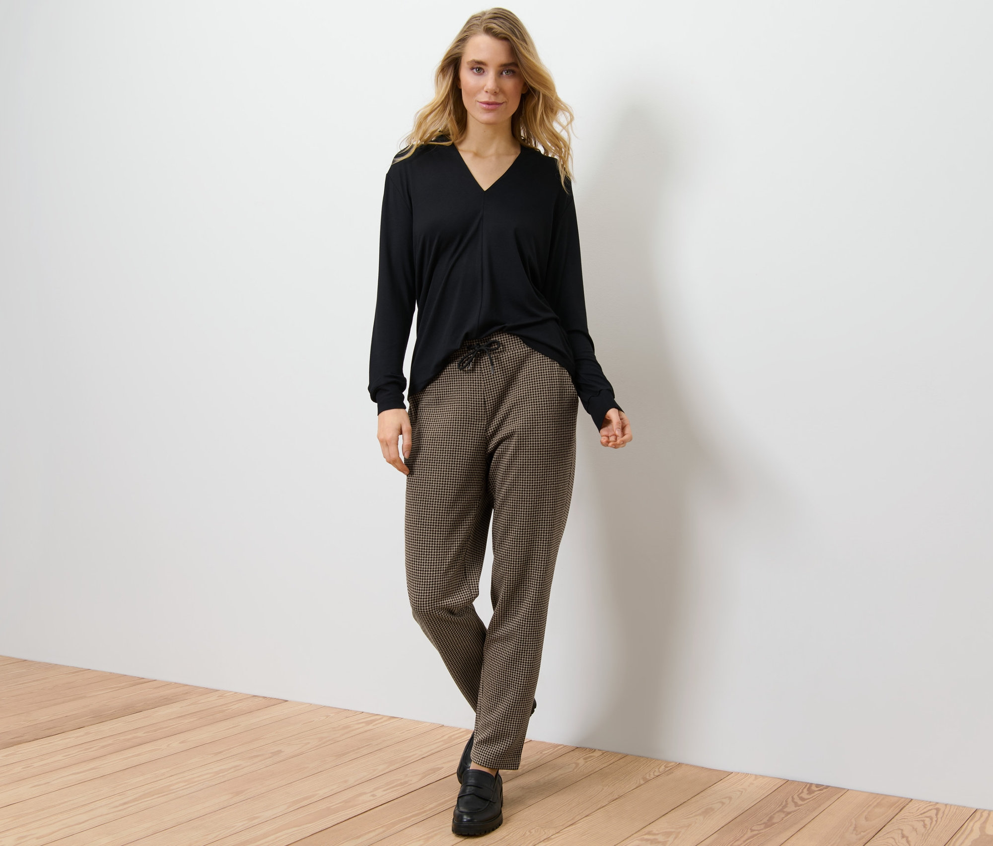 Blonde Frau posiert in schwarzem Oberteil und Joggpants mit Hahnentritt-Jacquard.