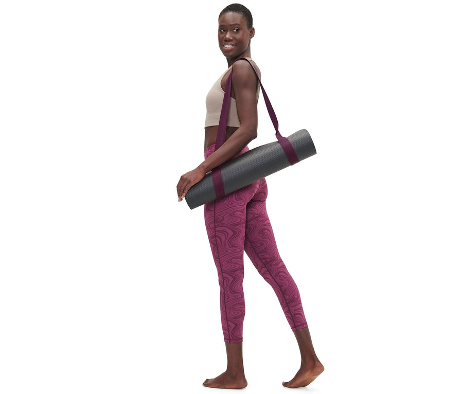 Frau geht mit 2-in-1-Yogagurt über der Schulter, der eine graue Yogamatte hält.