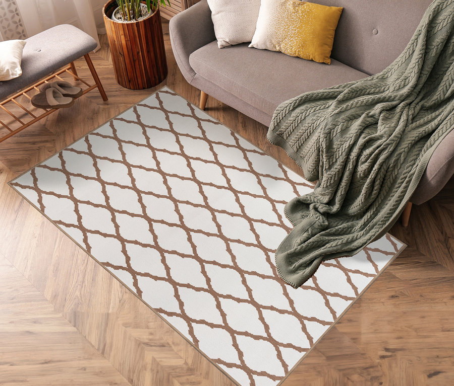Ein brauner und weisser Outdoor-Wendeteppich »Rhombus« liegt auf einem Holzboden neben einem grauen Sofa.