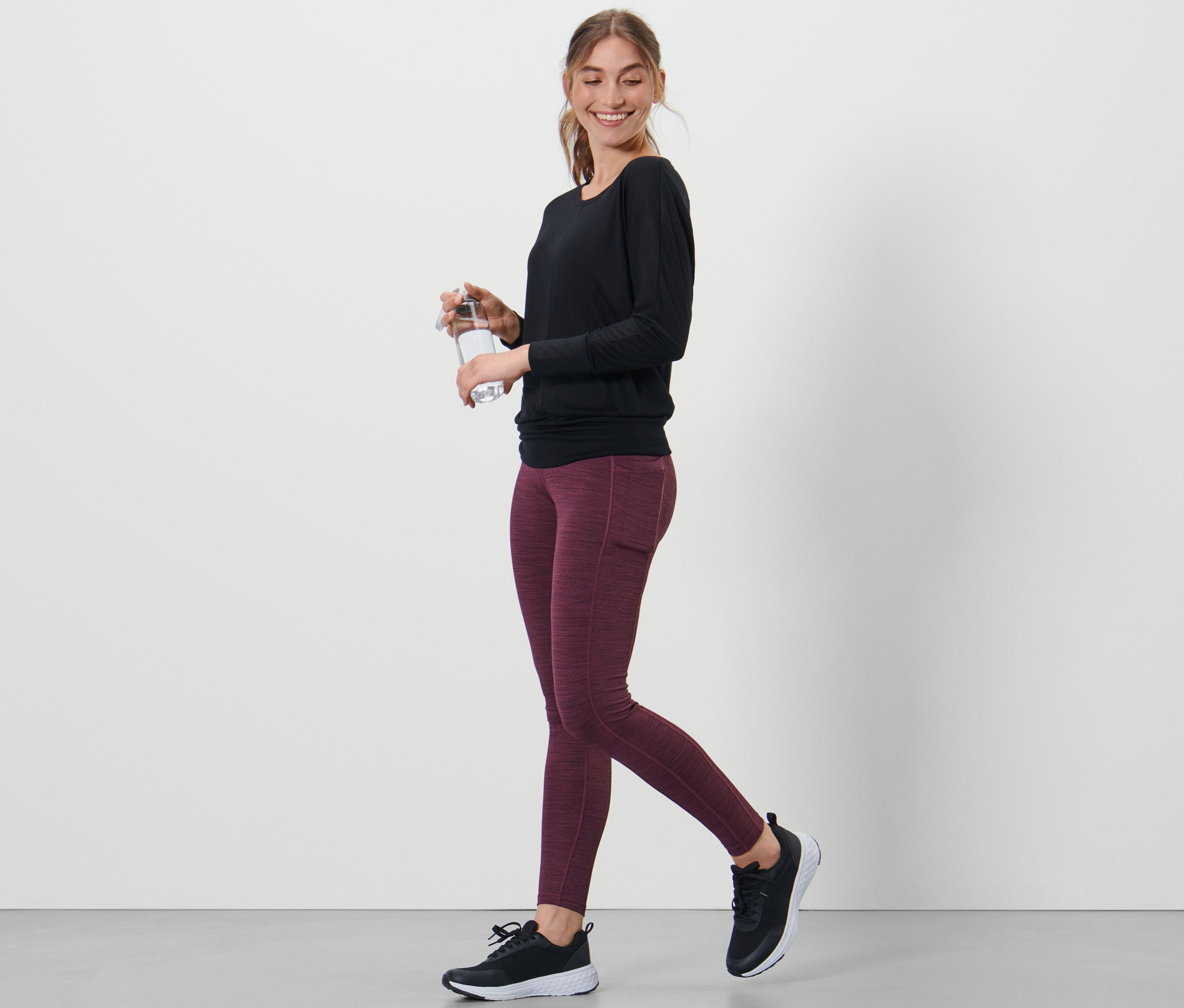 Frau geht und hält eine Wasserflasche. Sie trägt eine Sporttight.