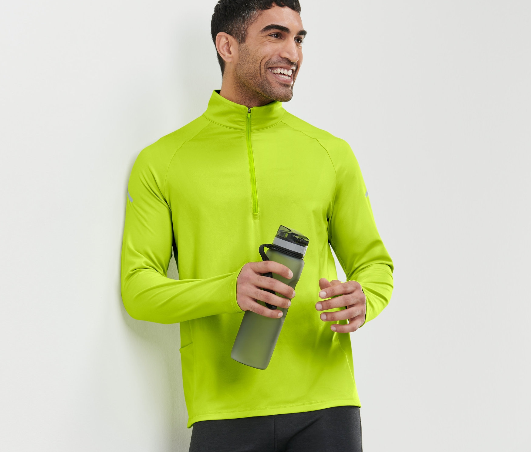 Mann lächelt und hält eine Wasserflasche, trägt ein neonlimes Thermo-Funktionsshirt.