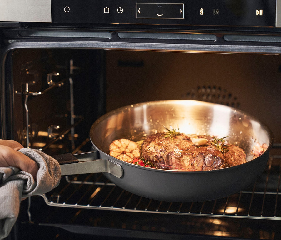 Mann schiebt ZWILLING Edelstahl-Bratpfanne, ca. 28 cm mit Braten in den Ofen.