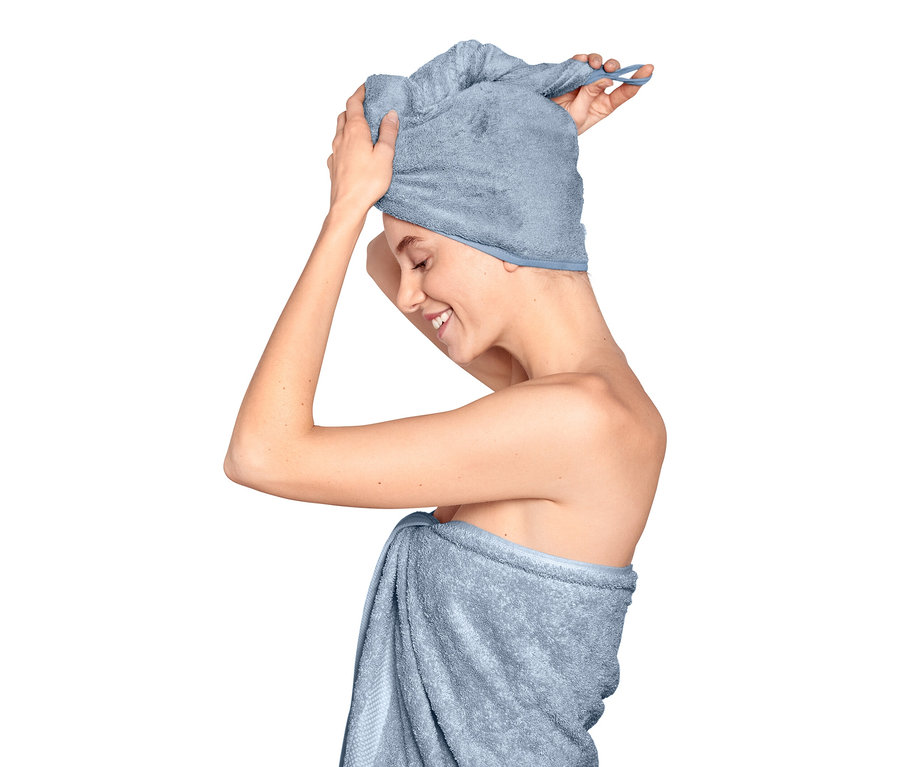 Frau richtet ein hellblaues Turban-Handtuch auf ihrem Kopf, ihr Körper ist in ein Handtuch gewickelt.
