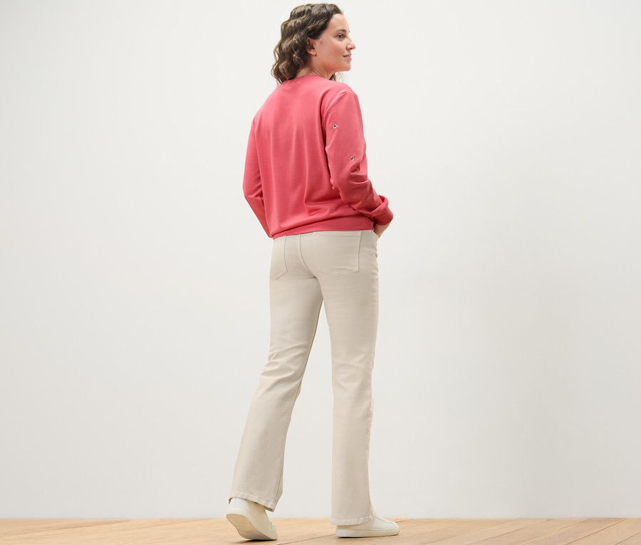 Eine Frau steht mit dem Rücken zur Kamera und trägt cremeweiße Bootcut Jeans ‒ Fit »Lou« und ein rosafarbenes Sweatshirt.