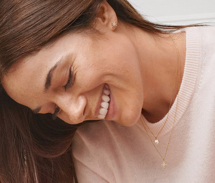 Eine lächelnde Frau trägt Gold-Ohrstecker Stern mit Zirkonia, Gold-Kette Stern mit Zirkonia und Gold-Kette mit Süßwasserzuchtperle.
