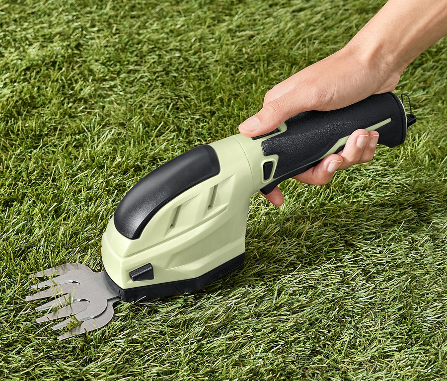 Hand hält Akku-Gartenschere auf Gras.