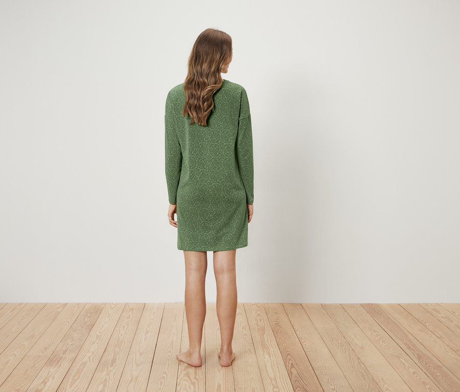 Frau steht mit dem Rücken zur Kamera und trägt ein grünes Kleid.