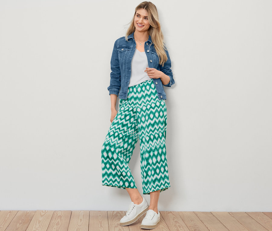 Blonde Frau posiert in Jeansjacke, weißem, strukturiertem Shirt und bedruckter Satinhose.