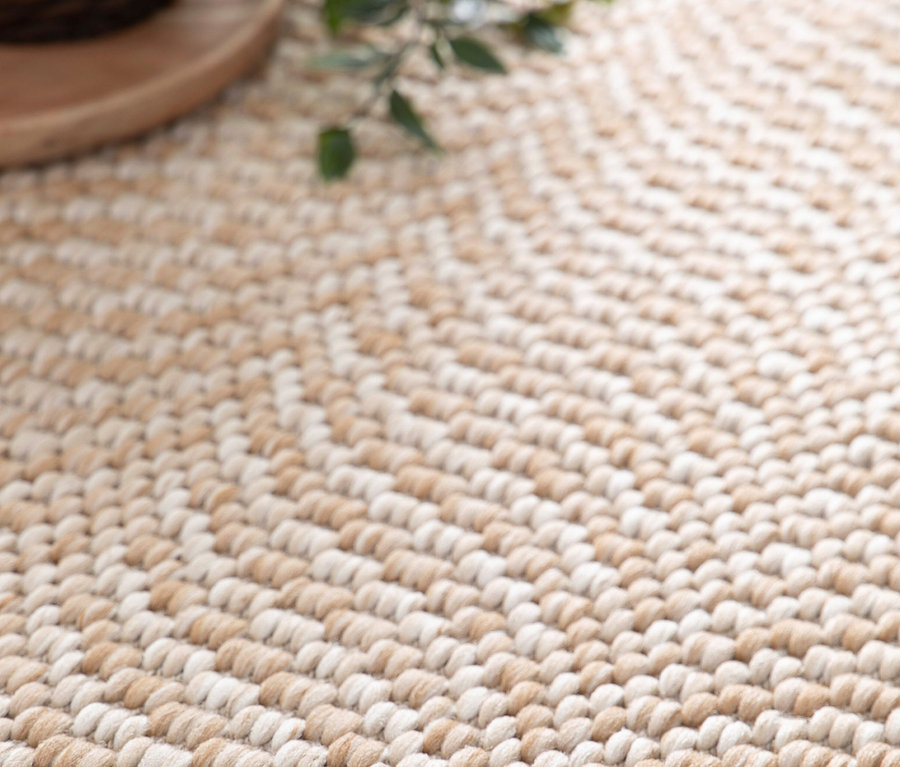 Detailaufnahme eines beigen Teppichs »Twine« mit Fischgrätenmuster.