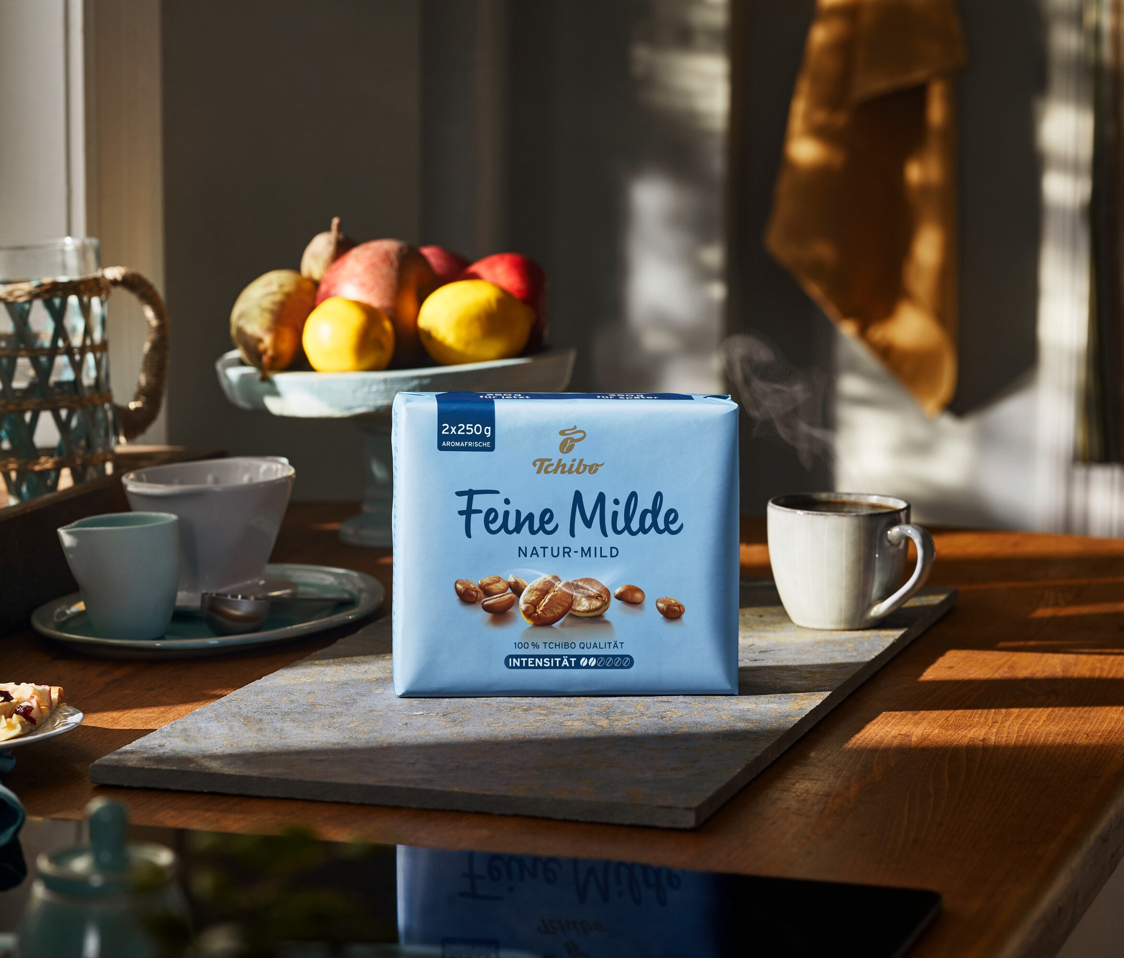 Eine Packung Feine Milde - 500 g Gemahlen steht auf einem Holztisch neben einer Tasse heißem Kaffee.