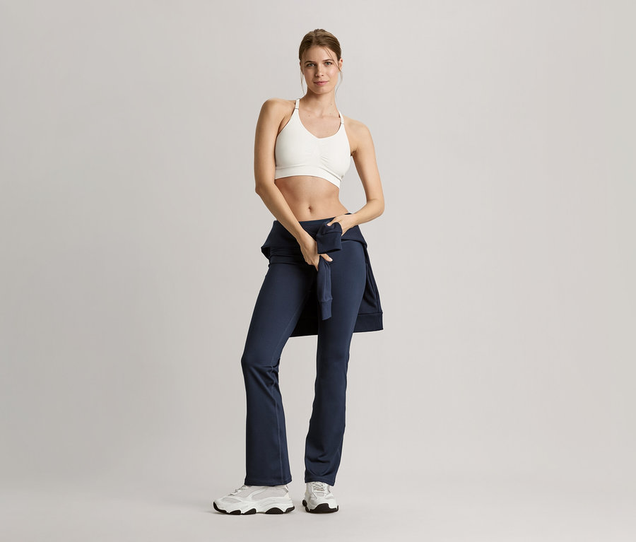 Frau in Sportbekleidung posiert mit einer marineblauen Sweatjacke.