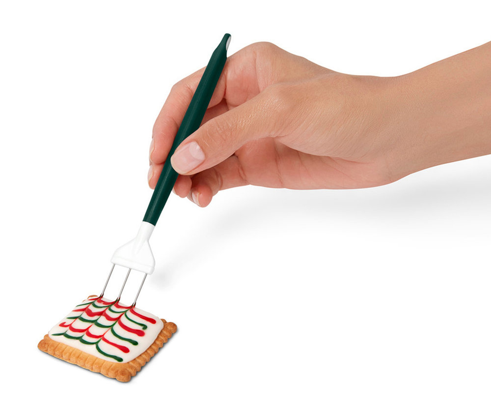 Eine Hand verziert einen Keks mit einem Dekorationswerkzeug.