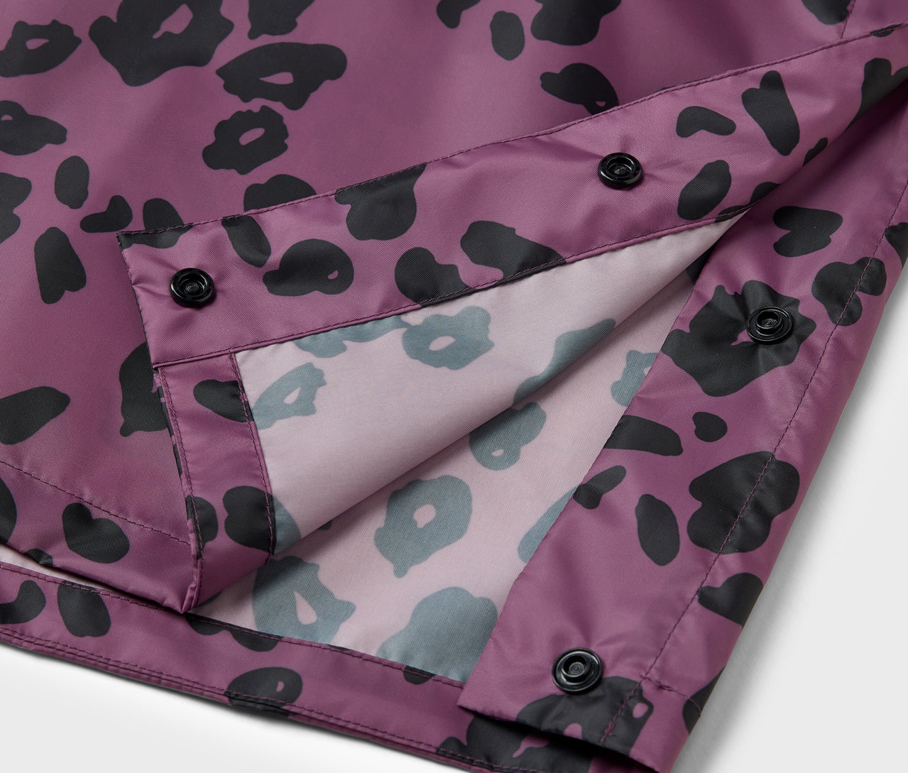 Detail einer lila Jacke mit schwarzem Tiermuster und schwarzen Knöpfen.