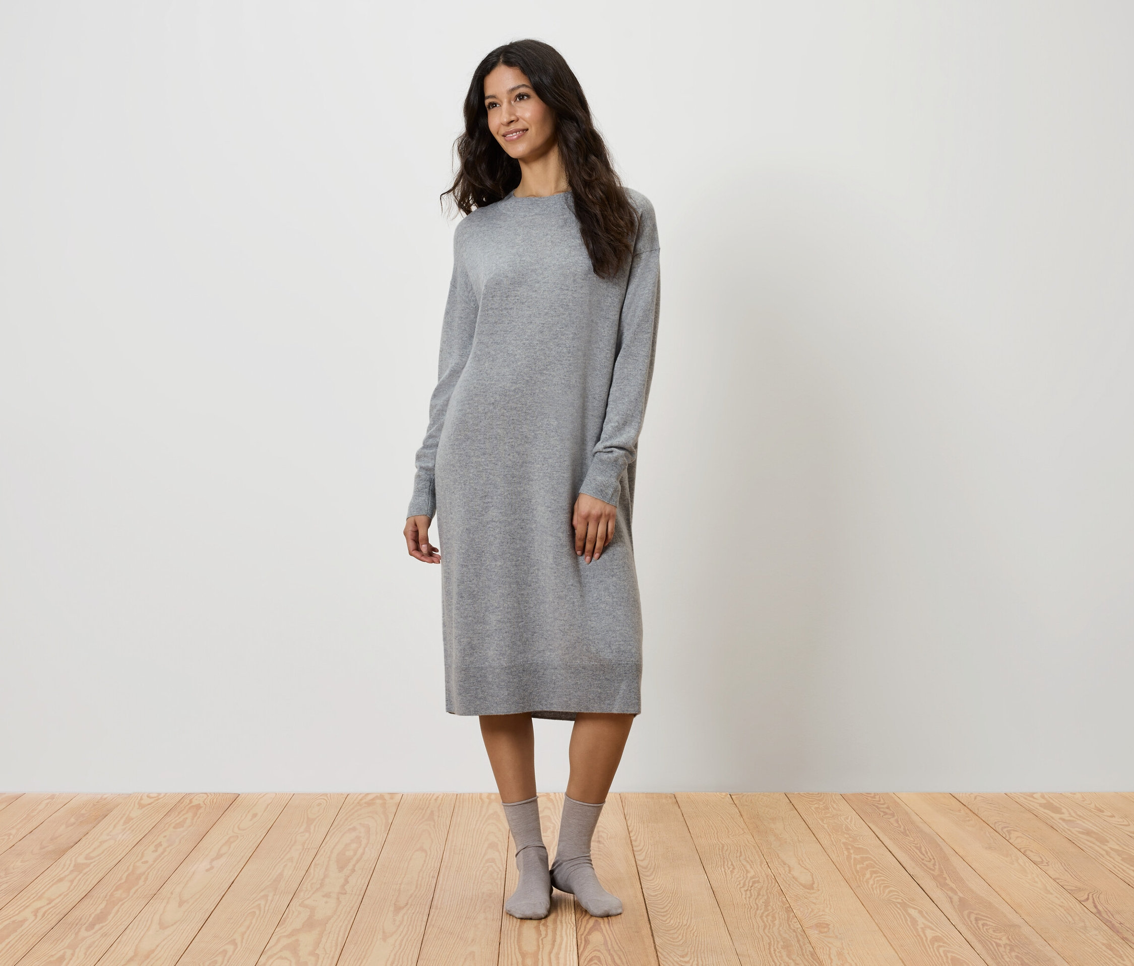 Frau steht in grauem Strickkleid und grauen Socken.
