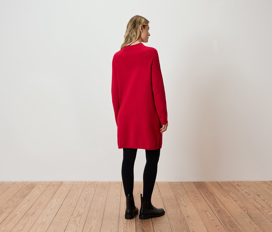 Eine Frau steht mit dem Rücken zur Kamera und trägt ein rotes Kleid, schwarze Leggings und schwarze Stiefel.