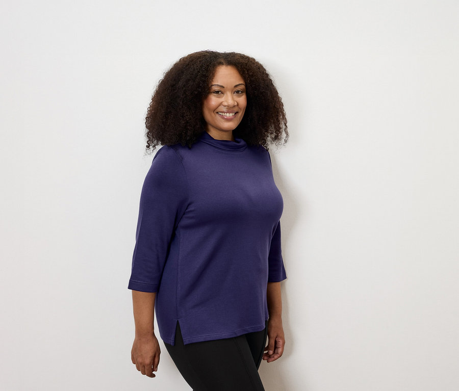 Frau trägt ein auberginefarbenes Sweatshirt mit Stehkragen und Heavy-Leggings mit Biese.