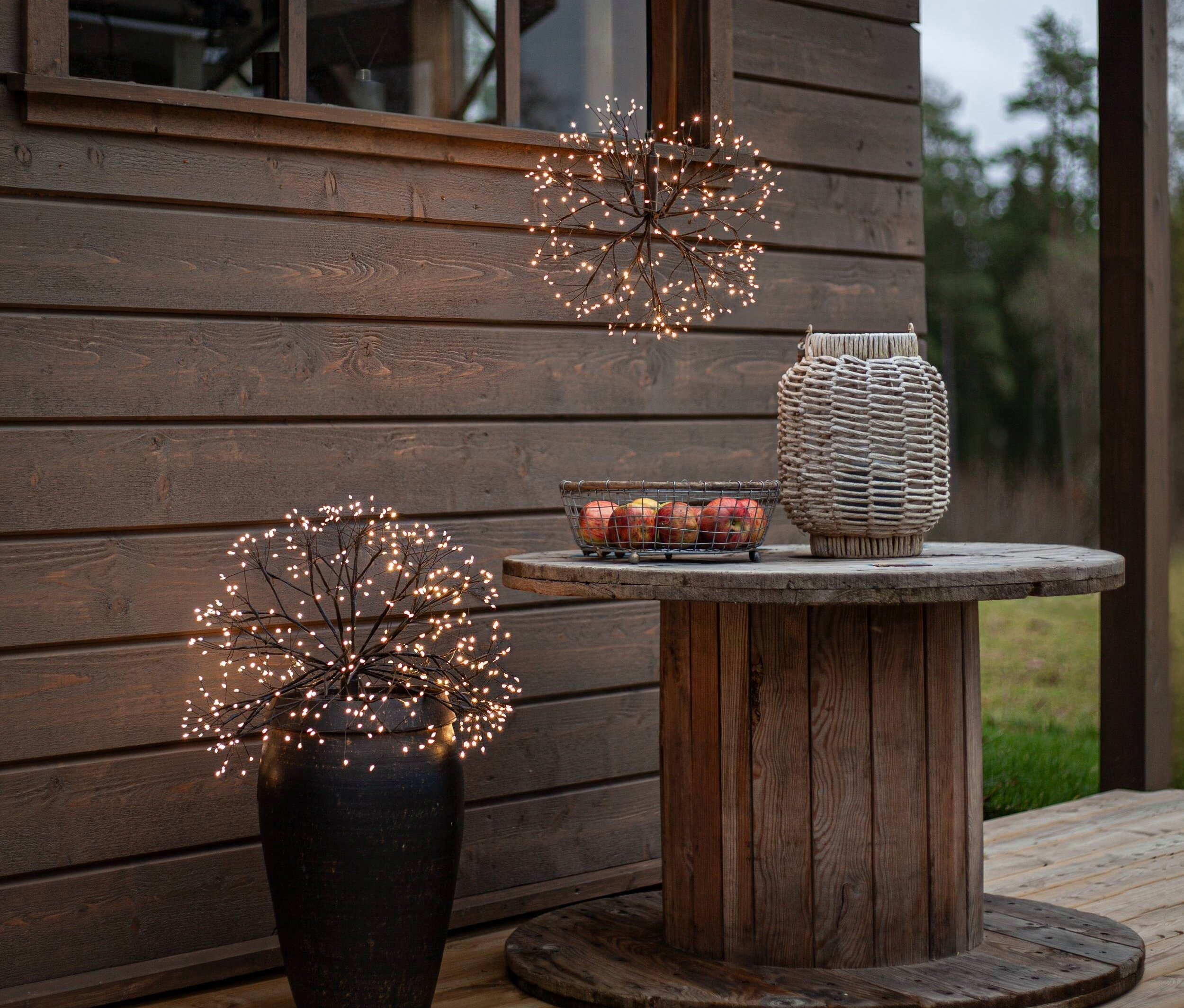 Zwei Lichterkugeln, eine hängend und die andere in einem Blumentopf, neben einem Holzgebäude.