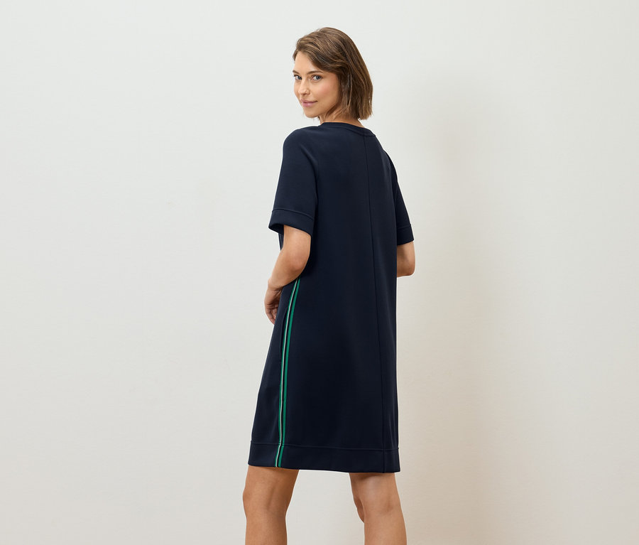 Frau blickt über die Schulter und trägt ein marineblaues T-Shirt-Kleid mit grünem Streifen.