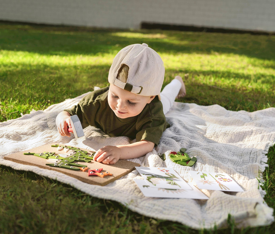 Kind spielt mit small foot Hämmerchenspiel, Pflanzen und Lebewesen auf einer Decke im Gras.