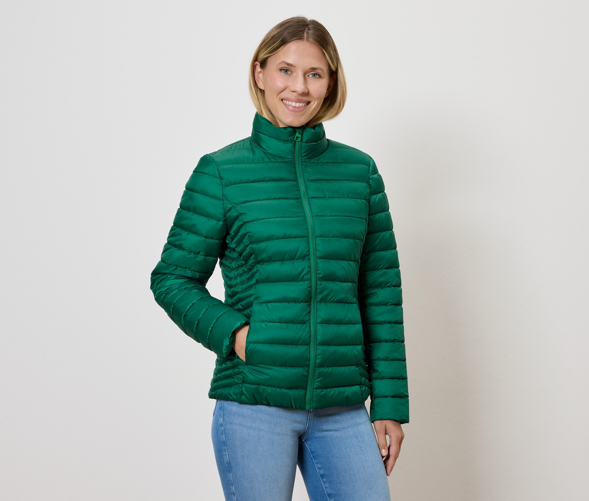 Frau trägt eine grüne Steppjacke und Jeans.