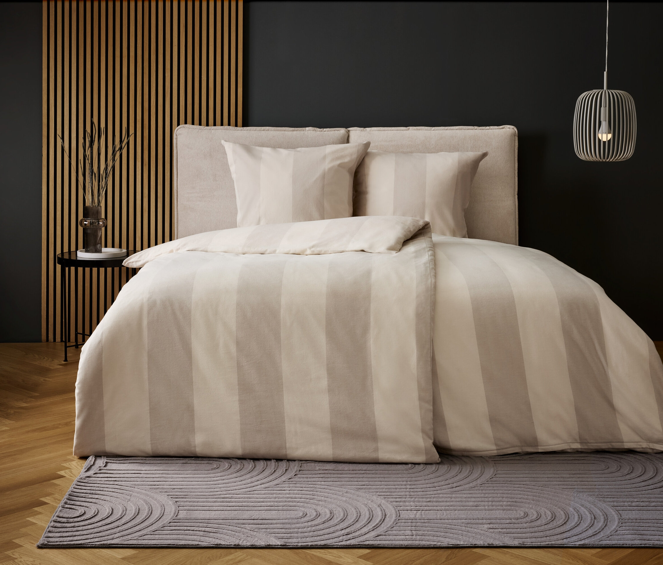 Schlafzimmer mit Bettwäsche mit beigen Streifen und grauem Teppich mit Kreismuster.