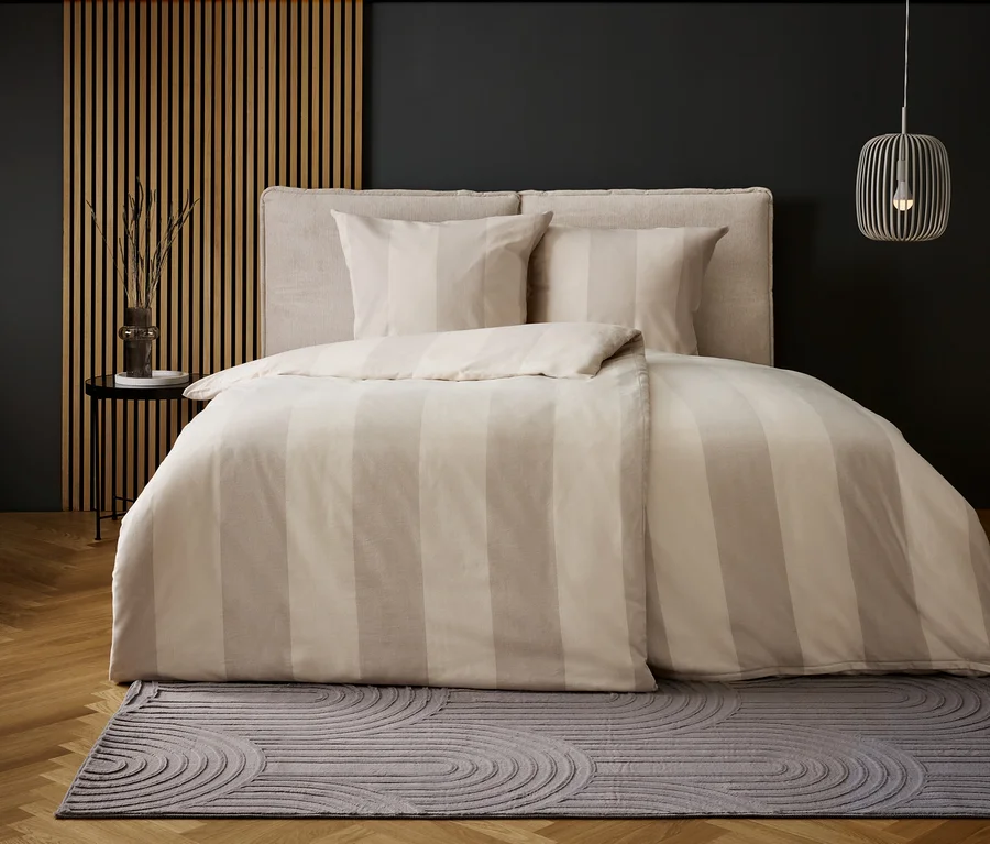 Schlafzimmer mit Bettwäsche mit beigen Streifen und grauem Teppich mit Kreismuster.