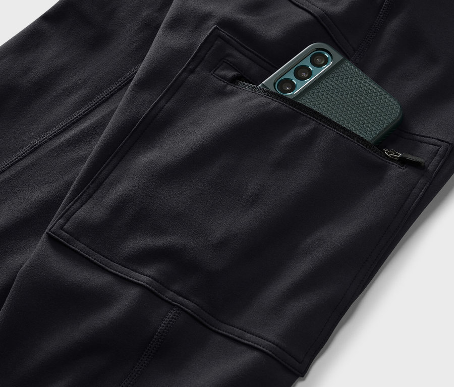Detailaufnahme einer schwarzen Outdoor-Tight mit einer Handytasche, in der sich ein grünes Handy befindet.