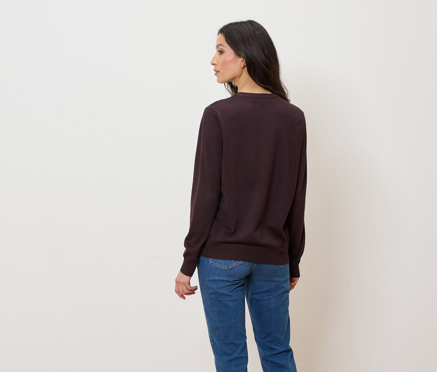 Frau trägt einen dunkelvioletten Pullover und blaue Jeans, von hinten gesehen.