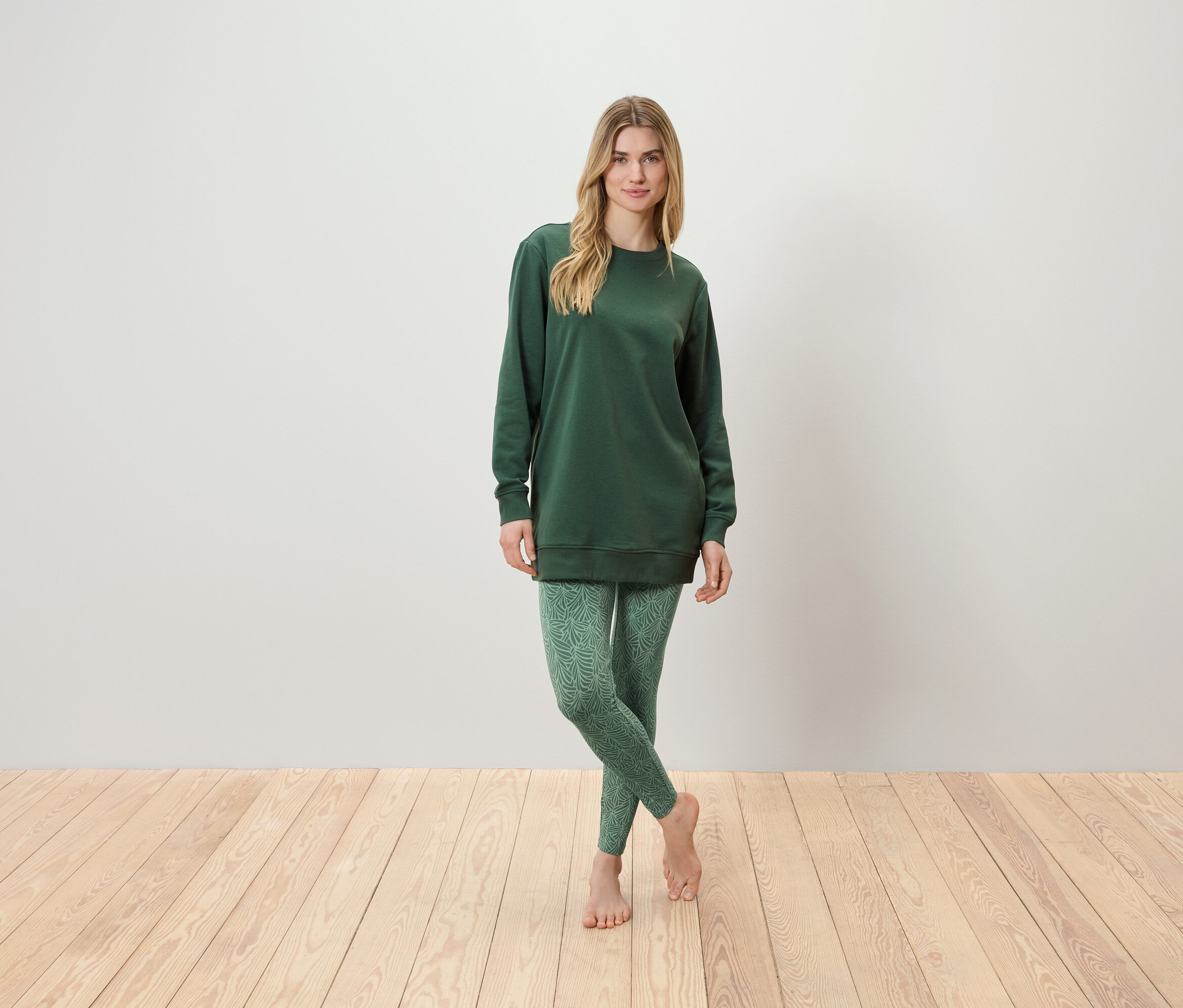 Frau steht und trägt eine grüne Tunika und grüne Leggings.