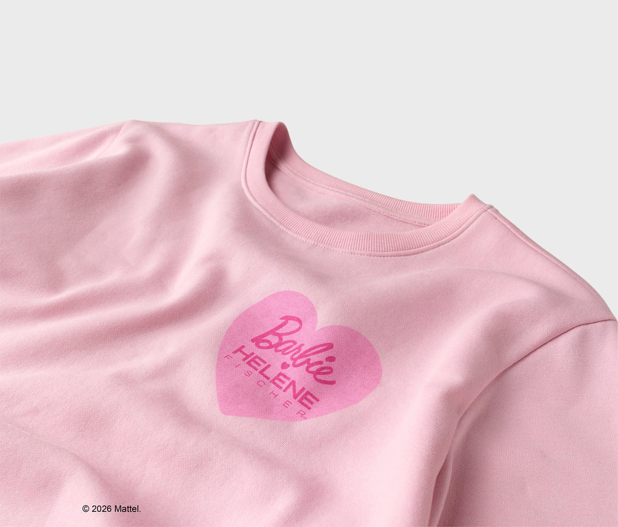 Detailansicht eines hellrosa Pullovers mit einem rosa Herzaufdruck mit dem Barbie-Logo und dem Namen Helene Fischer.