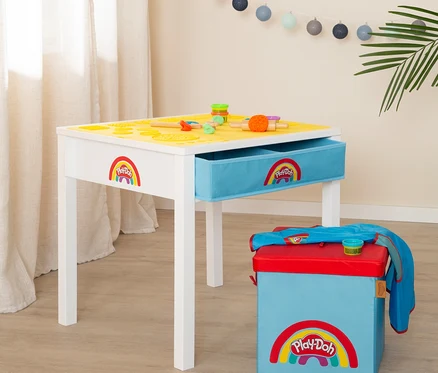 Ein weißer Spieltisch mit gelber Oberfläche und blauer Schublade, verziert mit dem Play-Doh-Logo, neben einer blauen Aufbewahrungsbox mit rotem Deckel.
