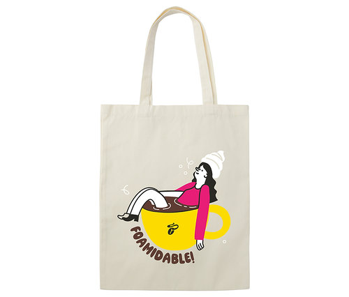 Eine Baumwolltasche "Foamidable" mit einer Illustration einer Frau, die in einer gelben Kaffeetasse liegt.