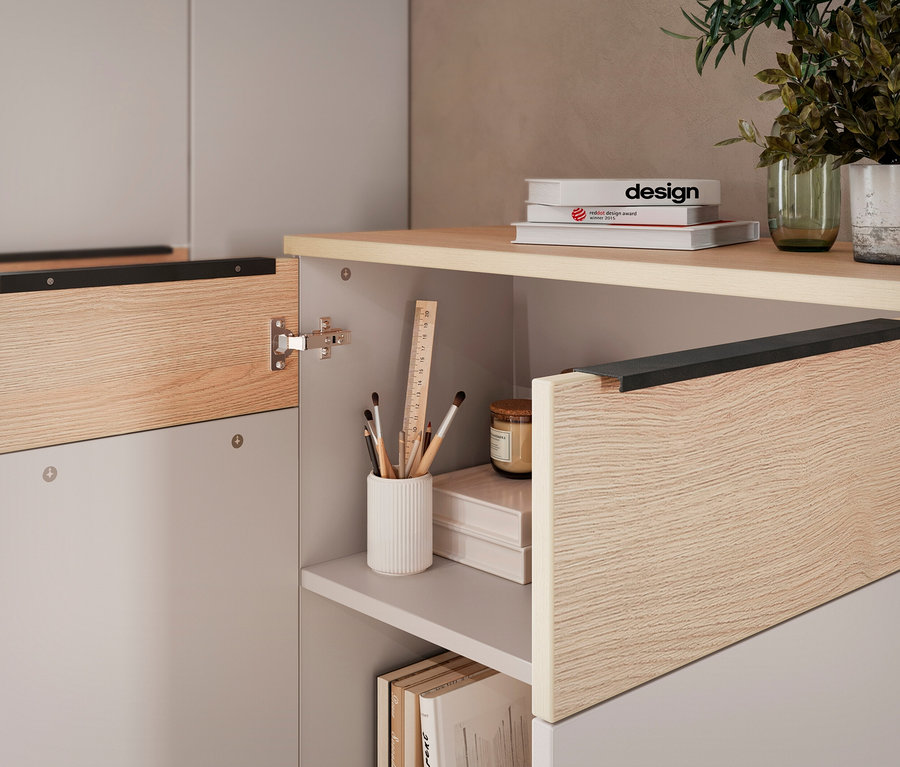 Detailansicht eines offenen Schranks mit Holztüren und Ablagefächern, auf denen Bücher, Stifte und eine Pflanze stehen.