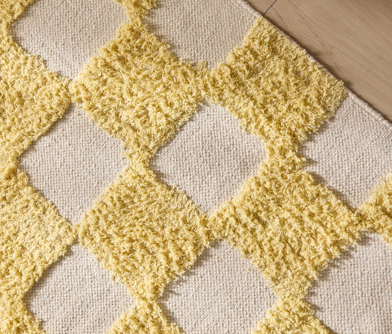 Nahaufnahme eines Teppichs mit gelben Rauten auf beigem Grund.