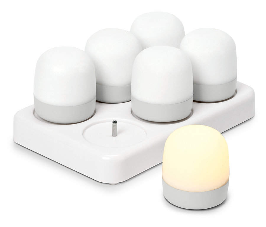 Fünf weiße, runde Nachtlichter in einer Ladestation, ein weiteres leuchtendes Nachtlicht steht daneben.