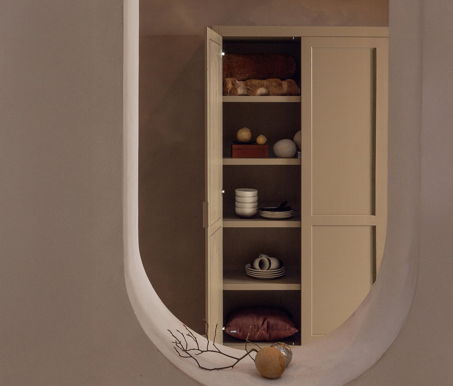 Blick durch einen ovalen Durchgang auf ein beigefarbenes Regal mit Textilien, Deko-Objekten und Geschirr.