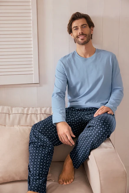 Ein Mann sitzt auf einem Sofa und trägt einen hellblauen Pullover und eine dunkelblaue Hose mit Punktmuster.