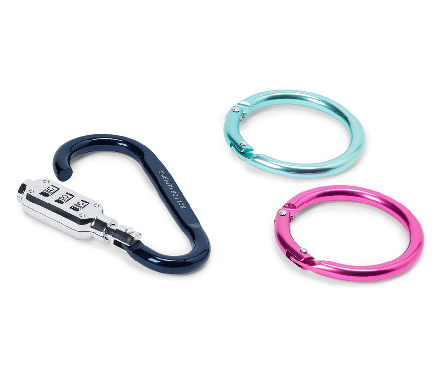 Drei Gegenstände liegen auf einer weißen Oberfläche: ein Karabiner mit Zahlenschloss in Schwarz und Silber und zwei Ringe, einer türkis, einer pink.