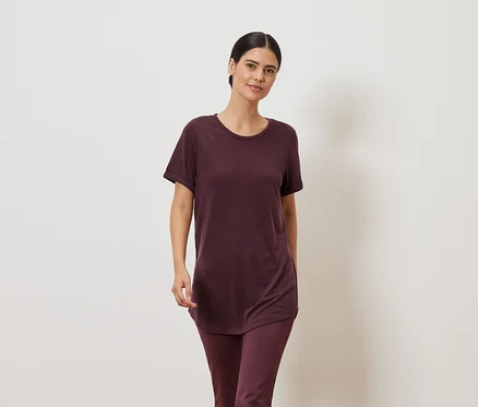 Frau in weinrotem T-Shirt und Leggings vor einem neutralen Hintergrund.